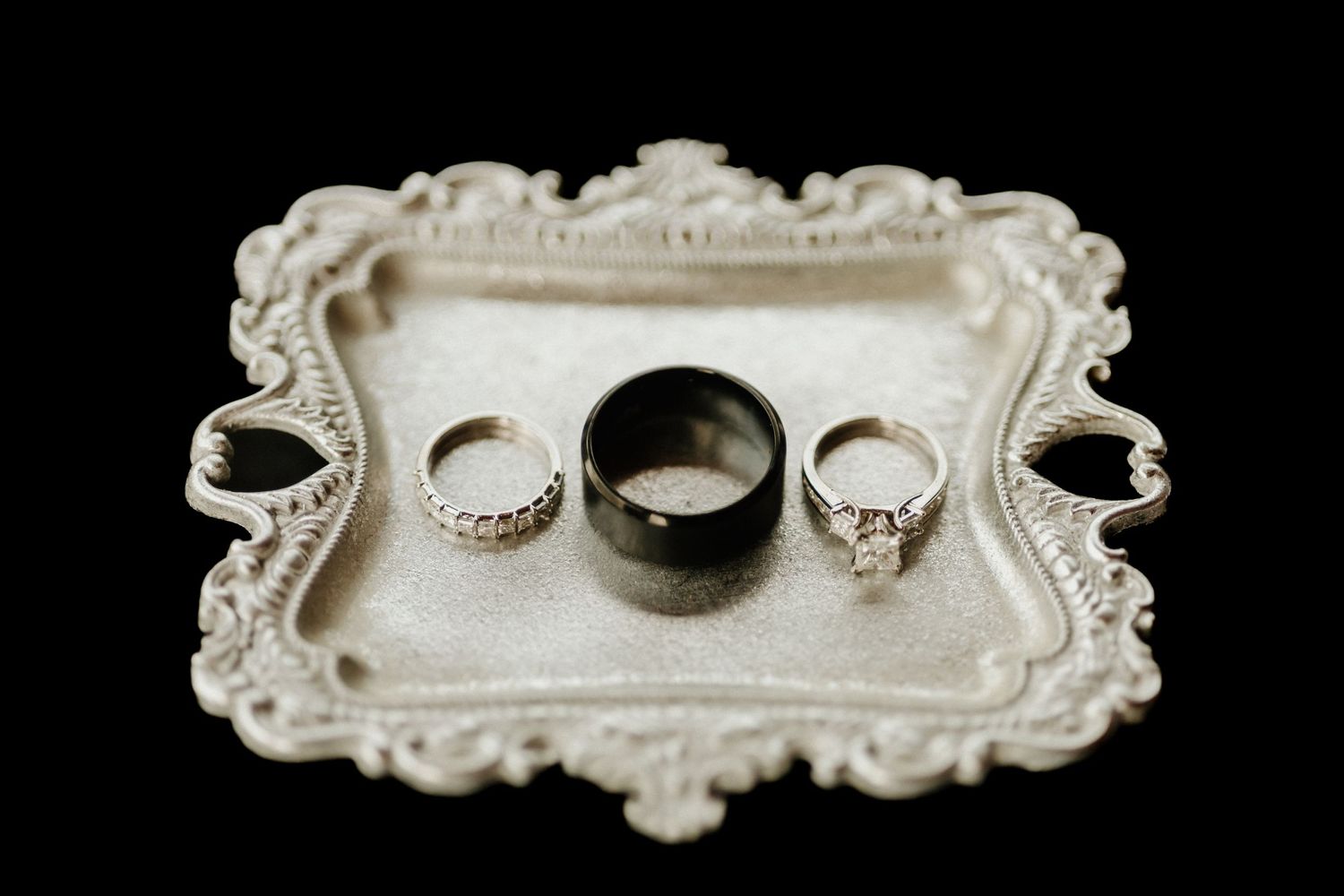 Wedding rings arranged on ornate vintage silver tray against dark background.