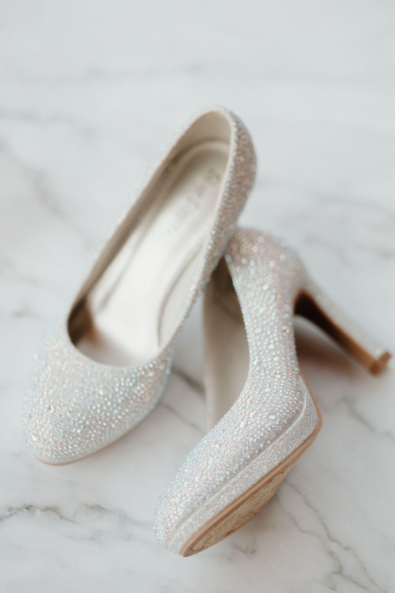 Sparkly white bridal heels with crystal embellishments on marble surface.