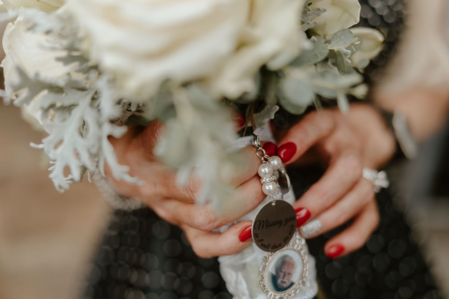 Close-up of hands holding white floral bouquet with red nail polish.