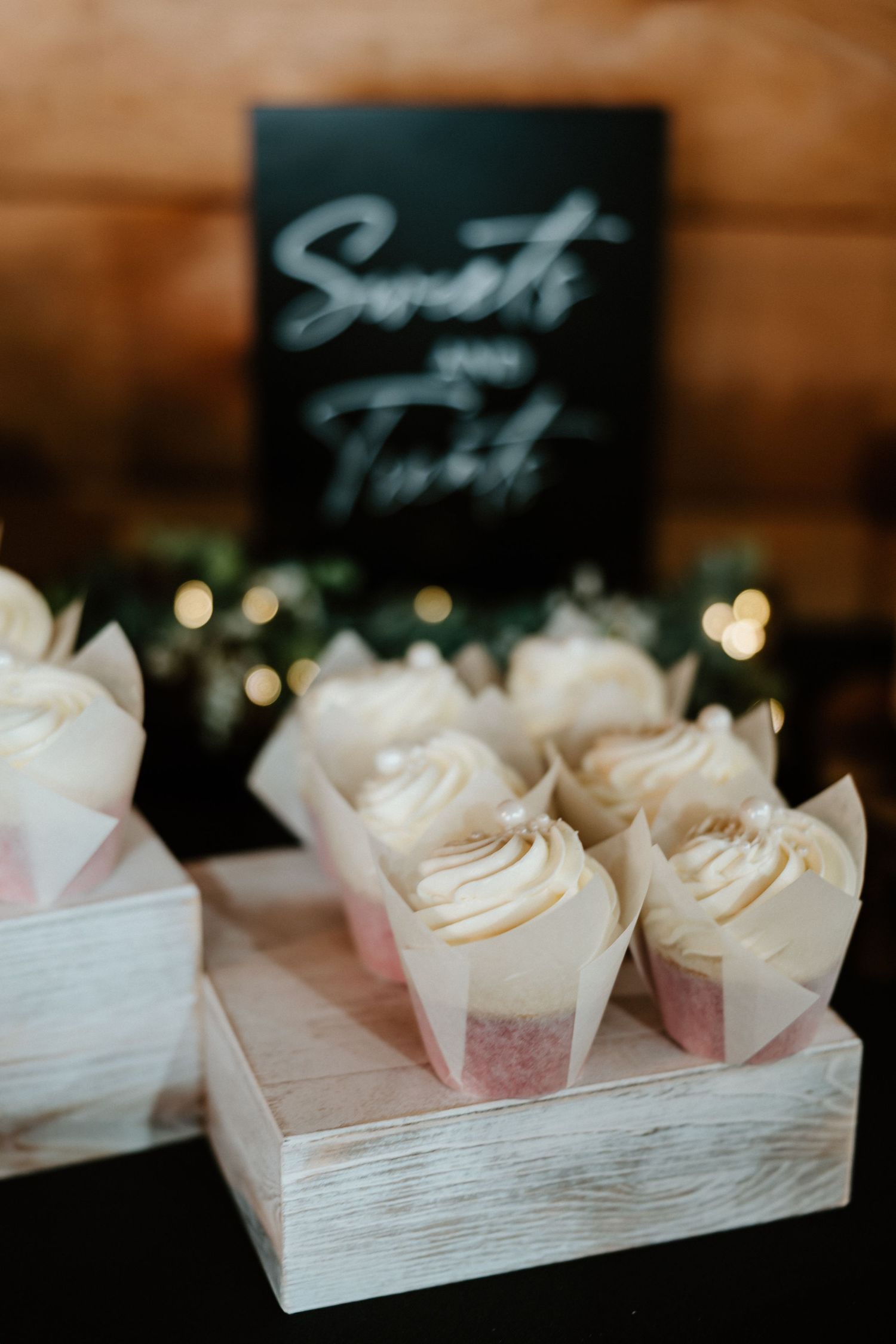 White frosted cupcakes displayed on rustic wooden stand at wedding dessert table.