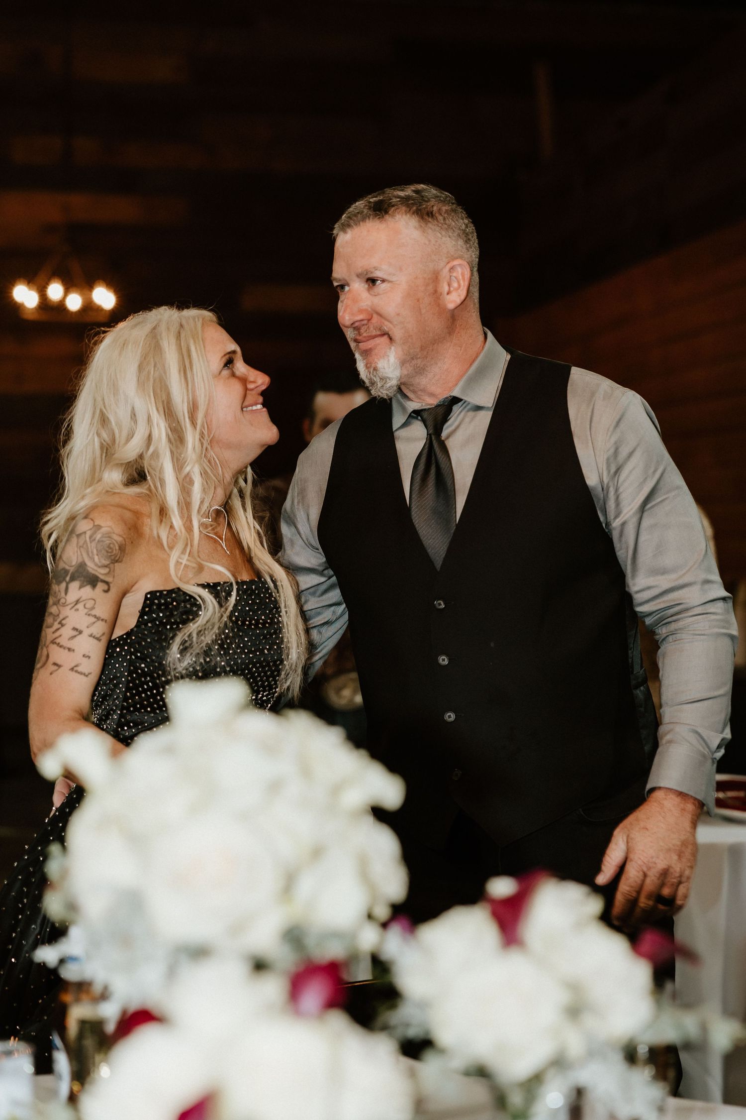 Couple sharing intimate moment at wedding reception with floral centerpieces on tables.