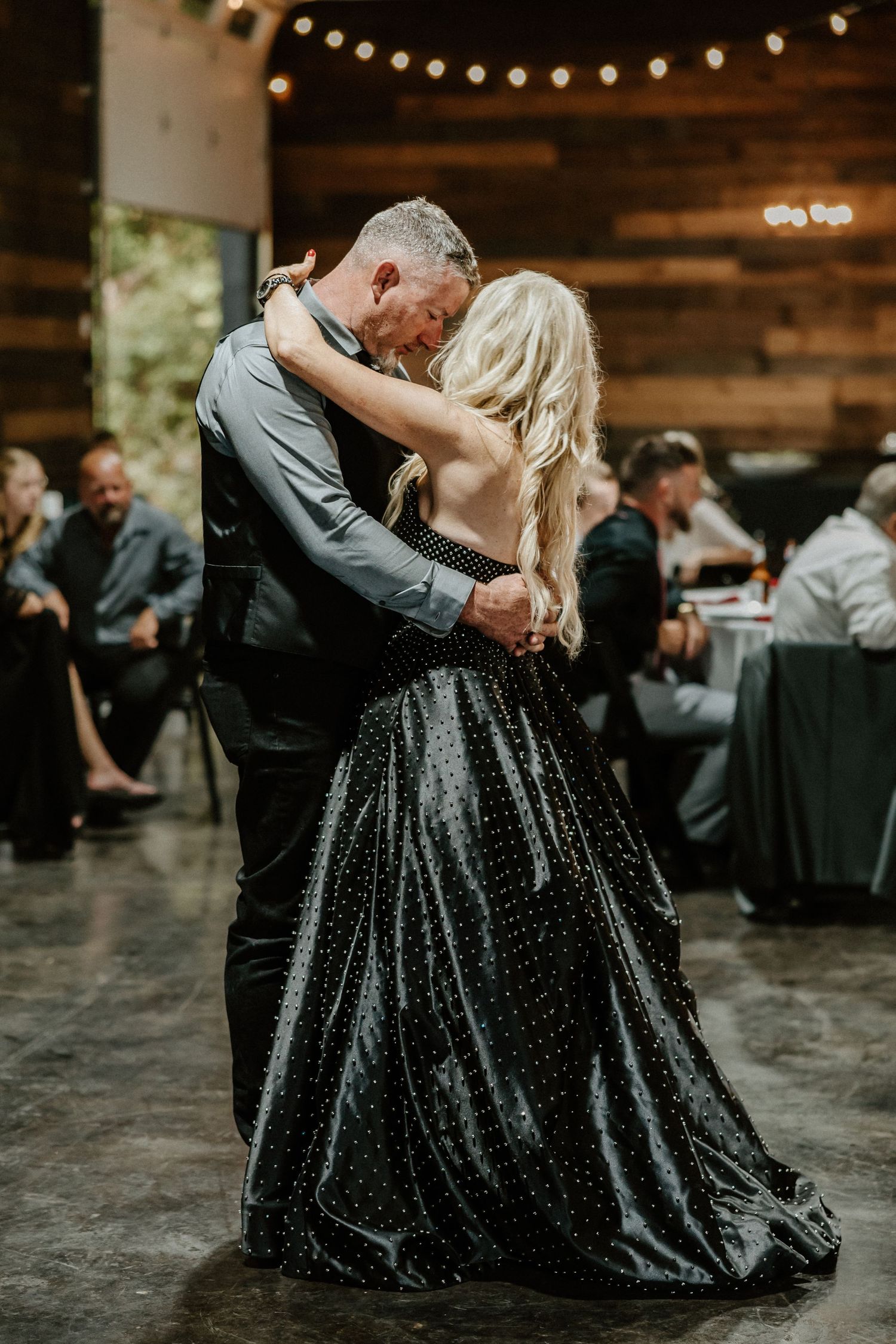 Dancing couple in formal attire under string lights at wedding reception.