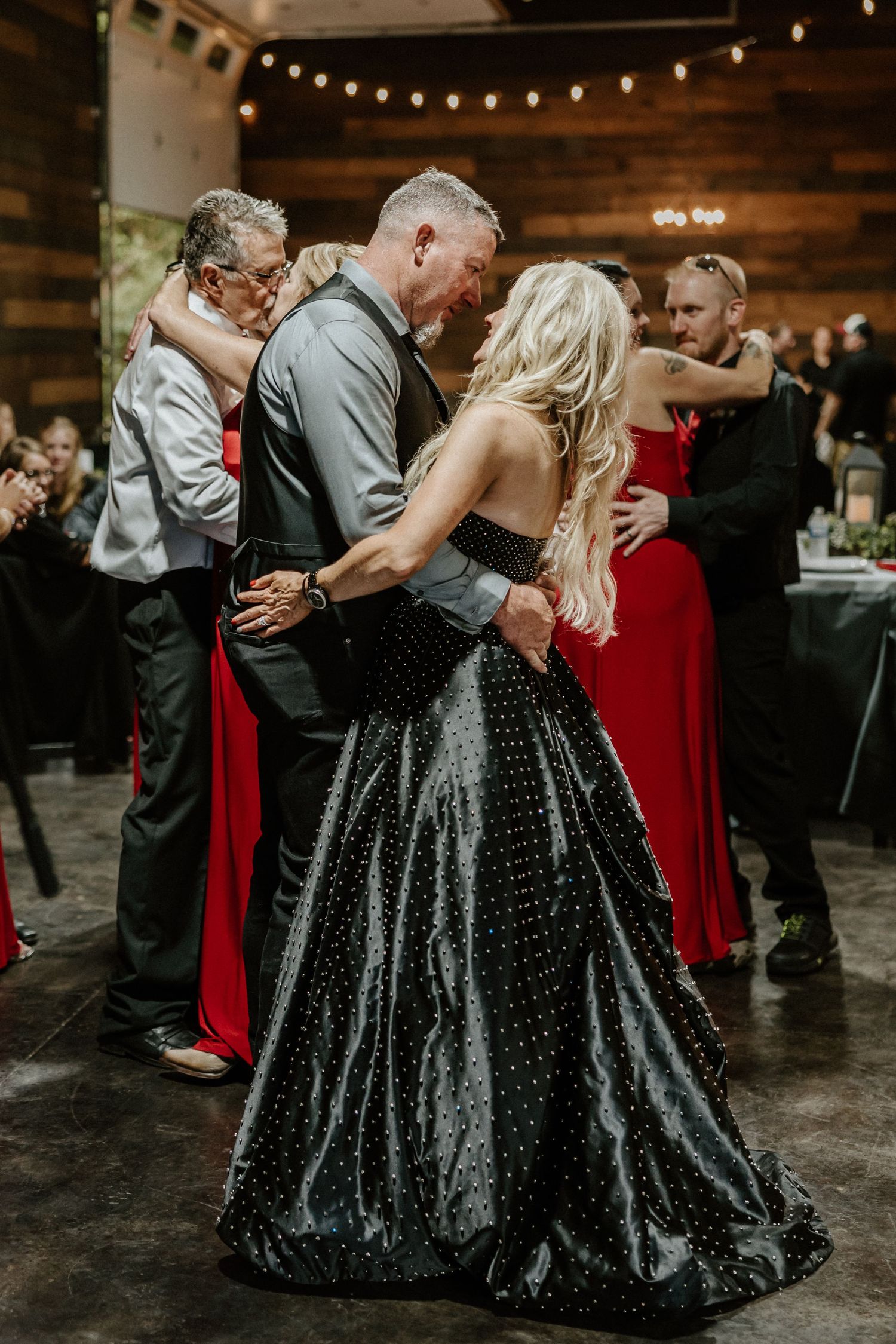 Couples dance intimately at an indoor reception venue with string lights and rustic decor.