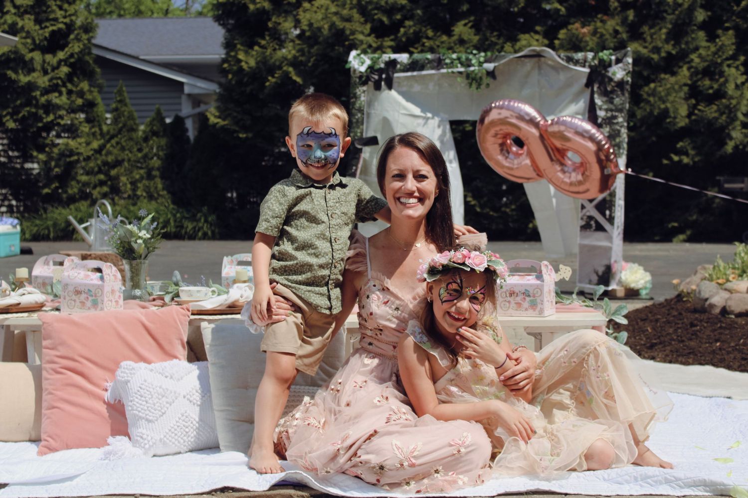 Family picnic outdoors with pink and peach decor on white blanket.