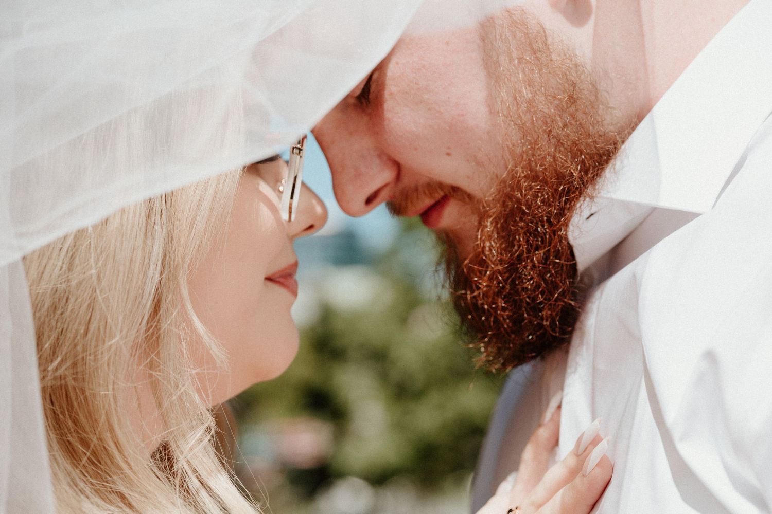 A tender romantic moment between a couple wearing white under a bridal veil.