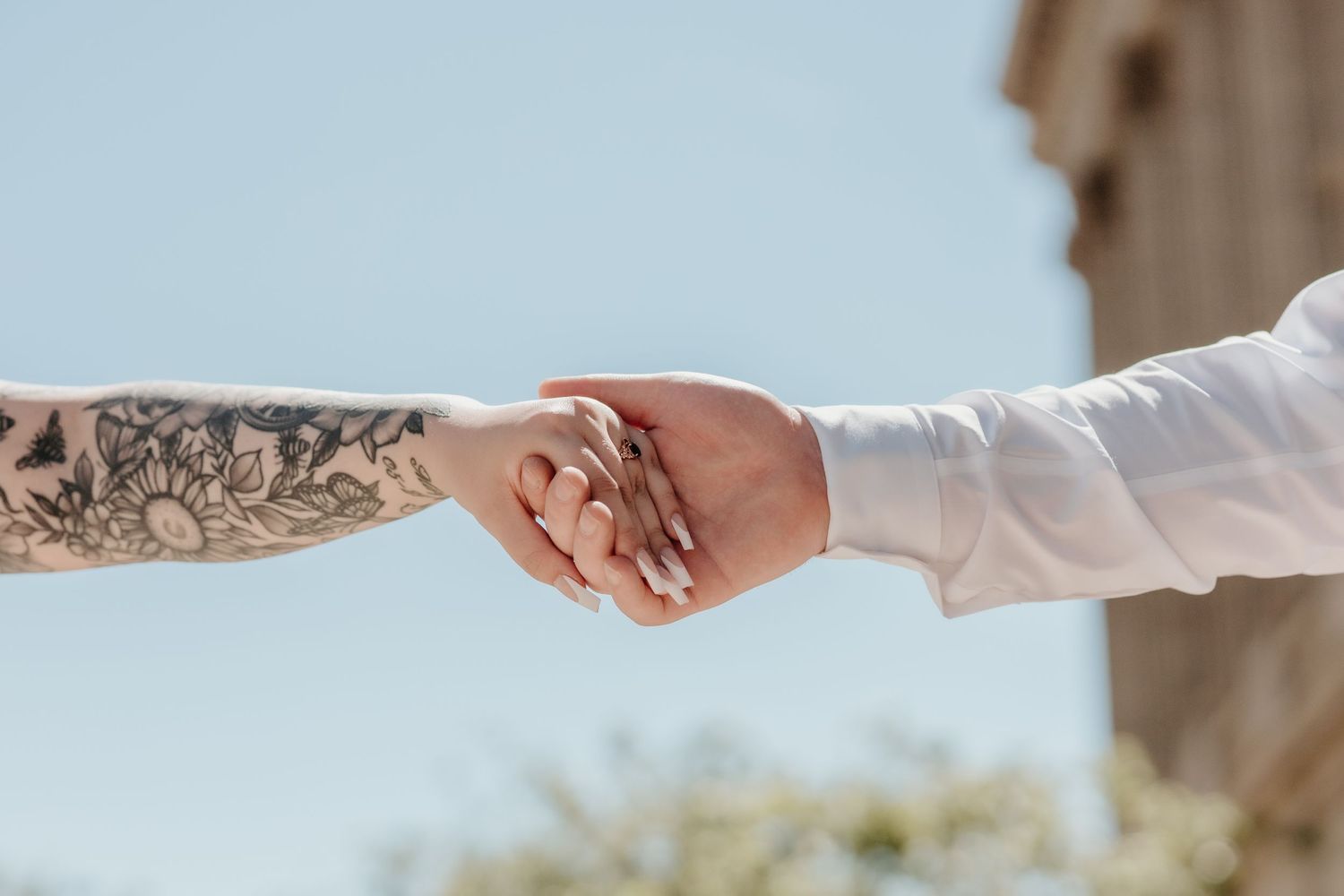 Two hands joining together in an intimate hold, with one arm showing detailed tattoo artwork.
