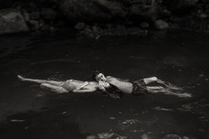 Black and white photo of a couple floating and embracing in a dark natural pool of water.