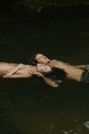 Two people floating peacefully together in a dark, tranquil natural body of water.