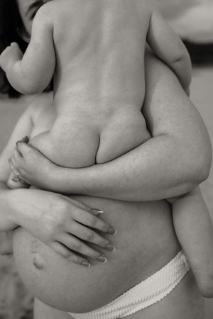 Black and white photo of pregnant woman holding a baby against her bare belly.