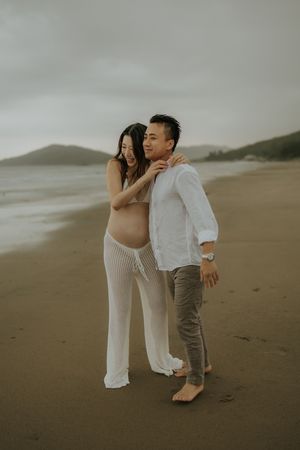 A couple in casual attire shares intimate moments while walking together on a misty beach.