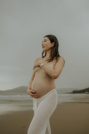 Moody beachside maternity photo shoot showing an artistic pregnancy silhouette against overcast skies.