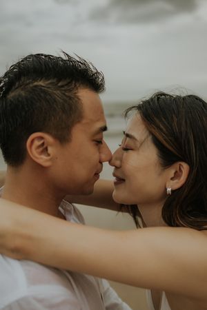 Romantic couple sharing an intimate moment outdoors with cloudy sky in background.