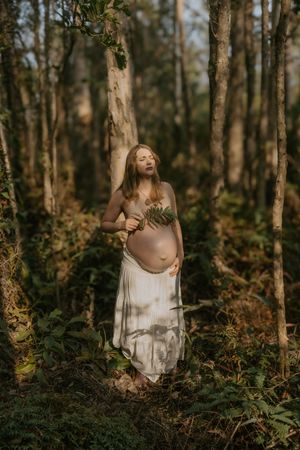 A person in a flowing white dress poses gracefully among trees in a dreamy forest setting.
