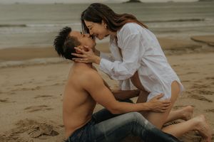 A romantic couple shares intimate moments on a sandy beach during a vintage-style sunset photoshoot.