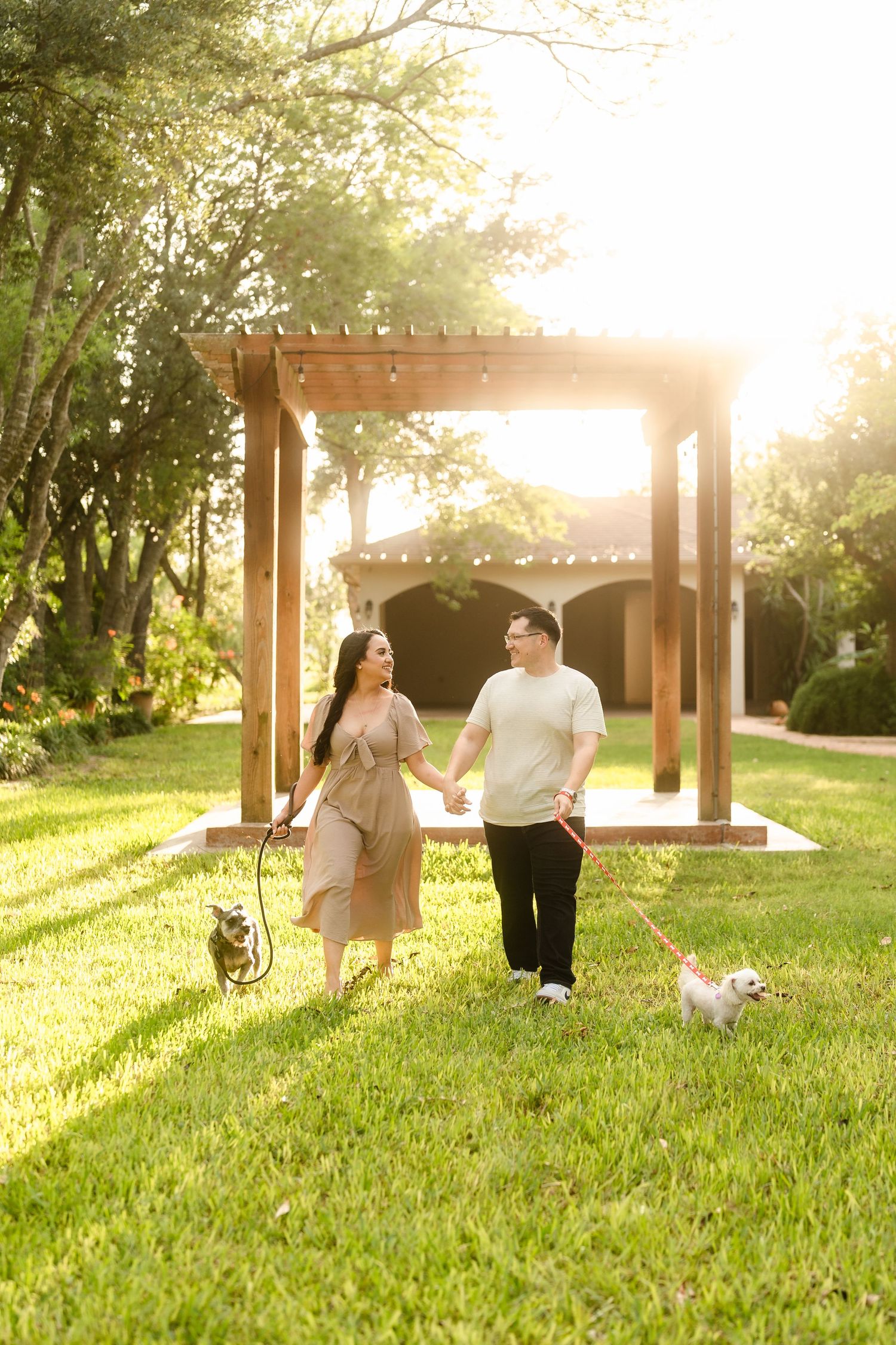 Pregnant woman in red floral dress kneeling on grass cradling her baby bump in golden sunset light.