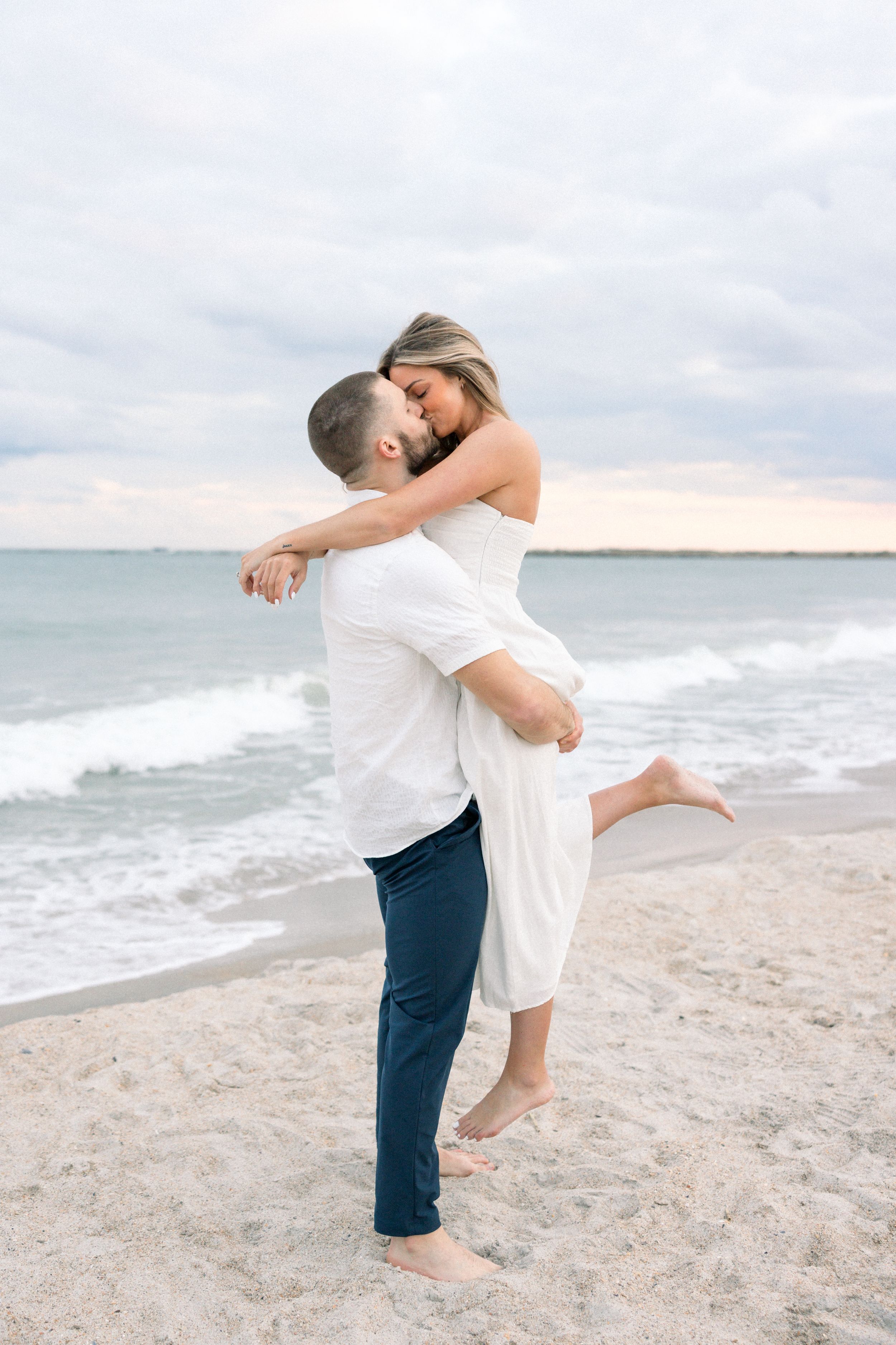 Romantic couple embracing on a sandy beach at sunset with ocean waves in the background.