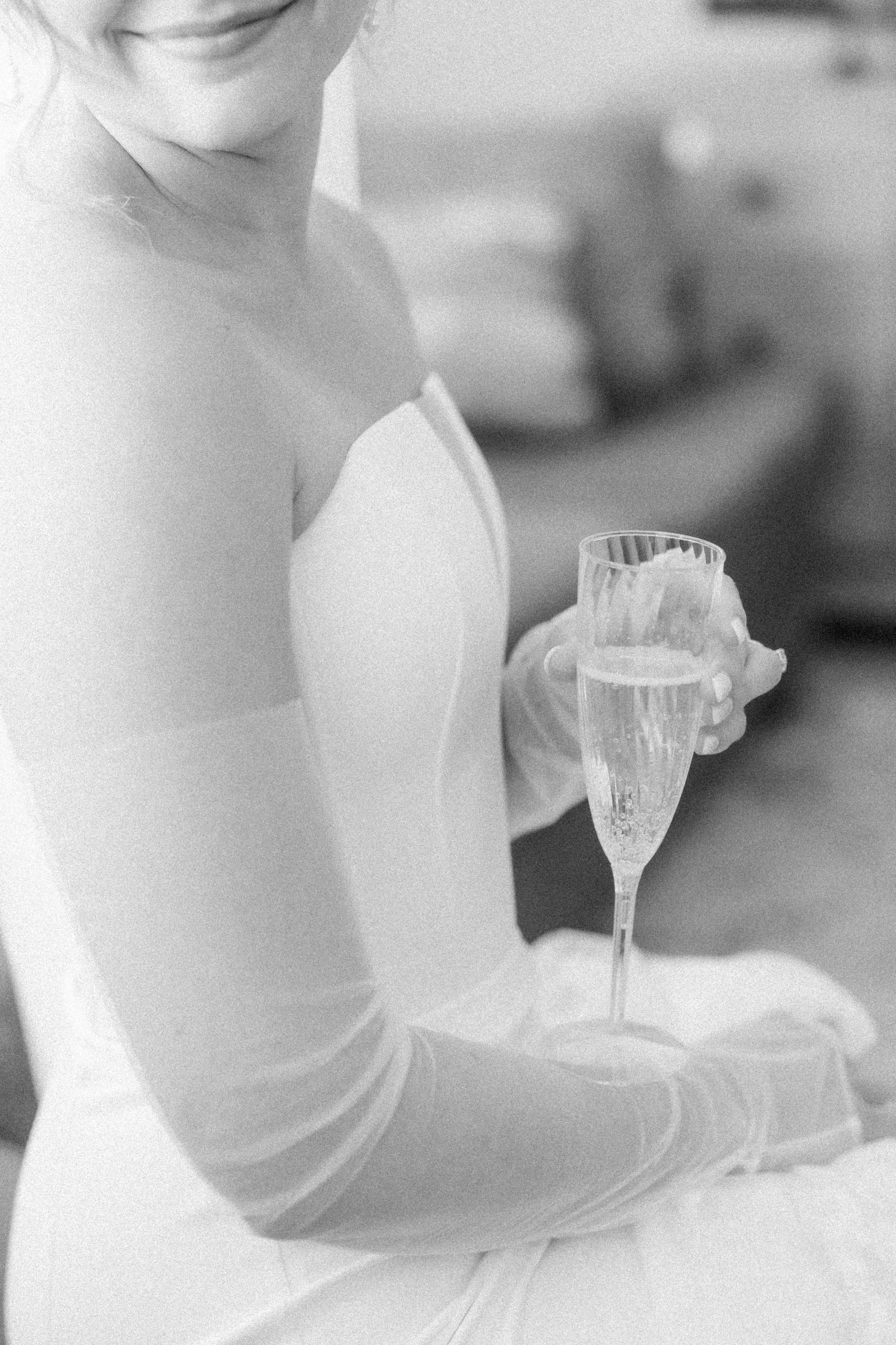 Close up of a bride in white gloves holding a delicate champagne flute in black and white.