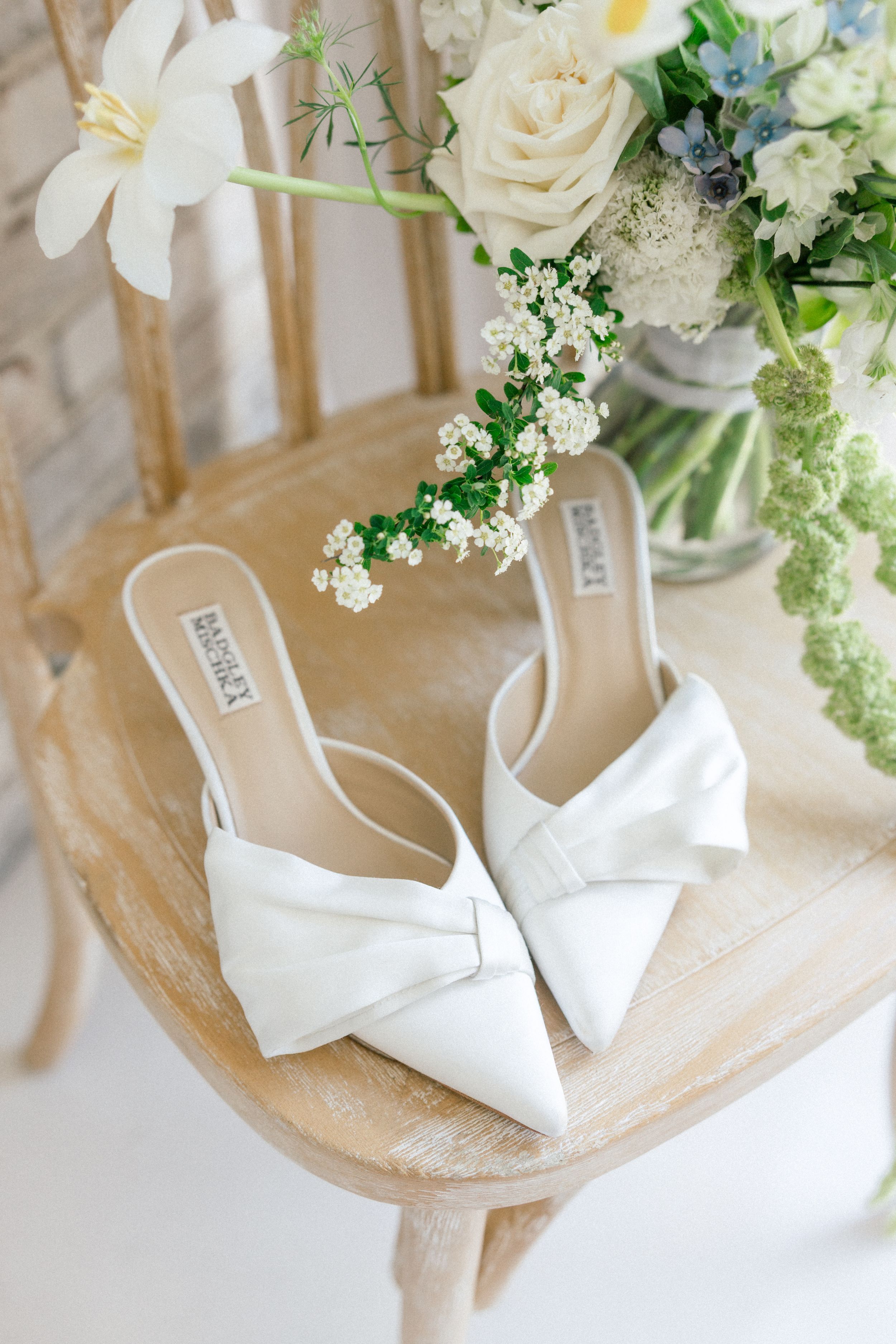 White bridal shoes and delicate floral arrangements with roses displayed on a light beige surface.