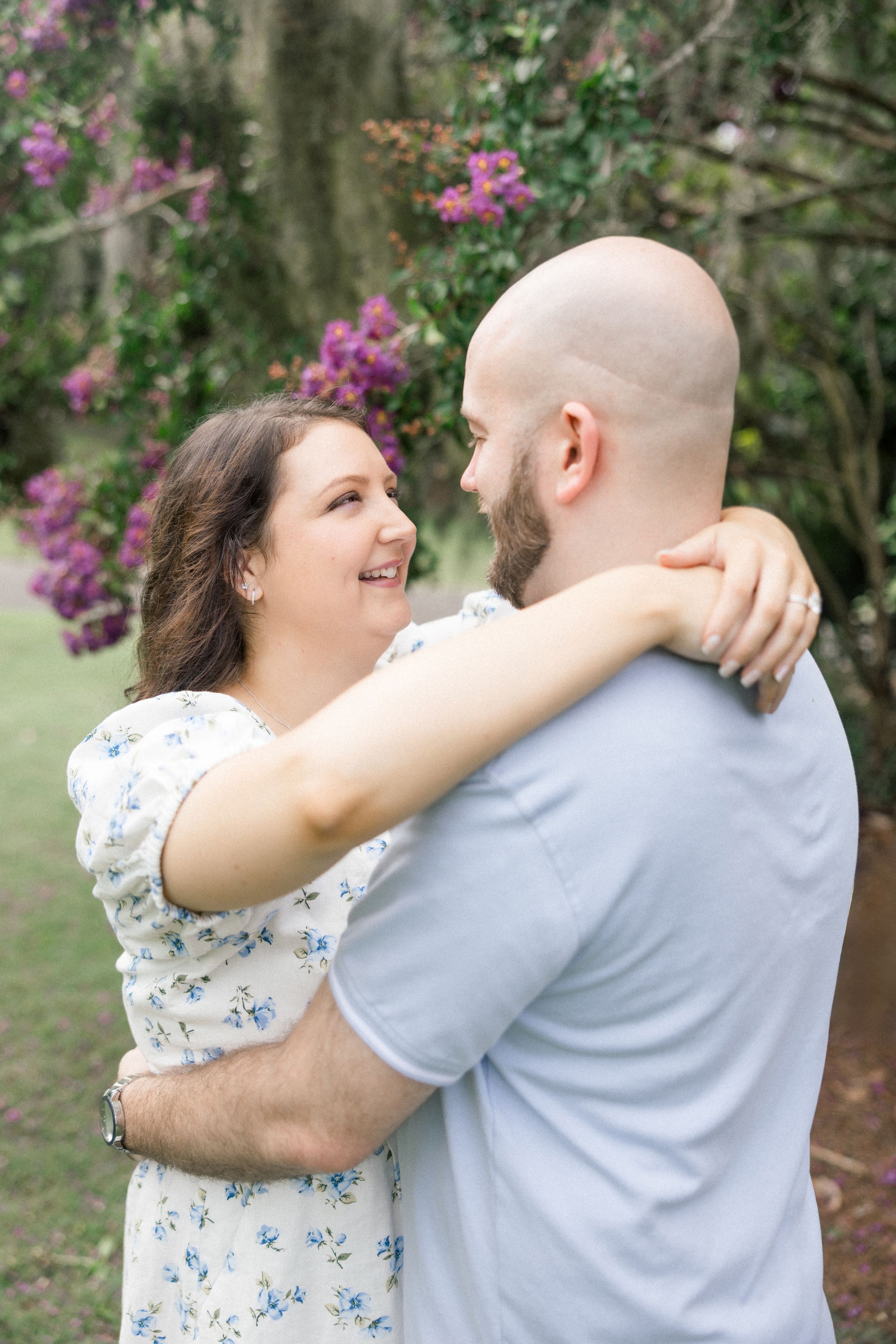 A couple shares a romantic moment outdoors surrounded by blooming pink flowers in a natural setting.