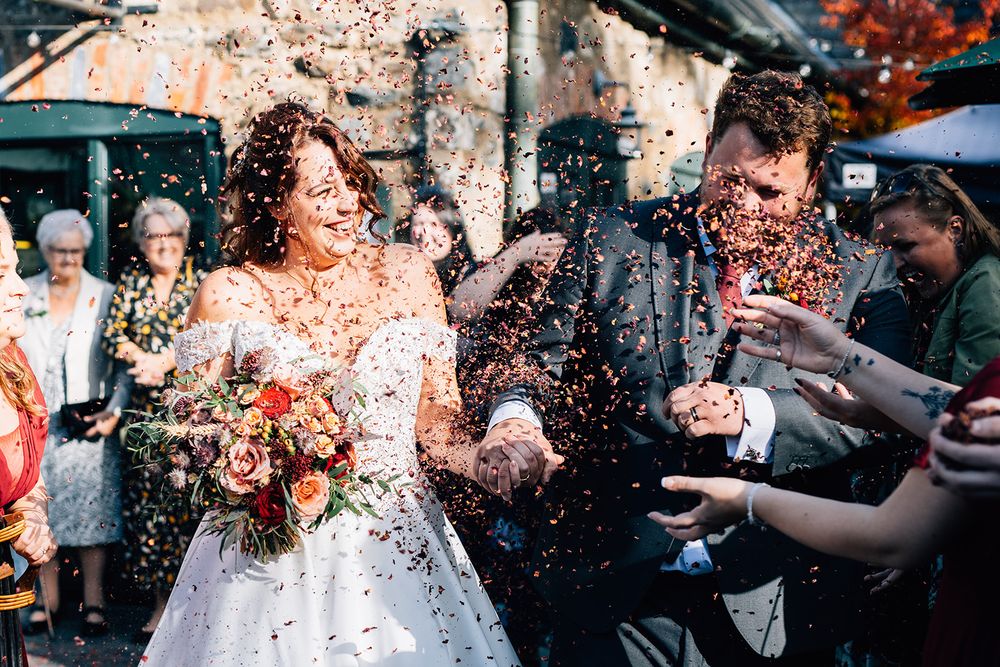 Wedding guests shower a couple with confetti during an outdoor celebration.