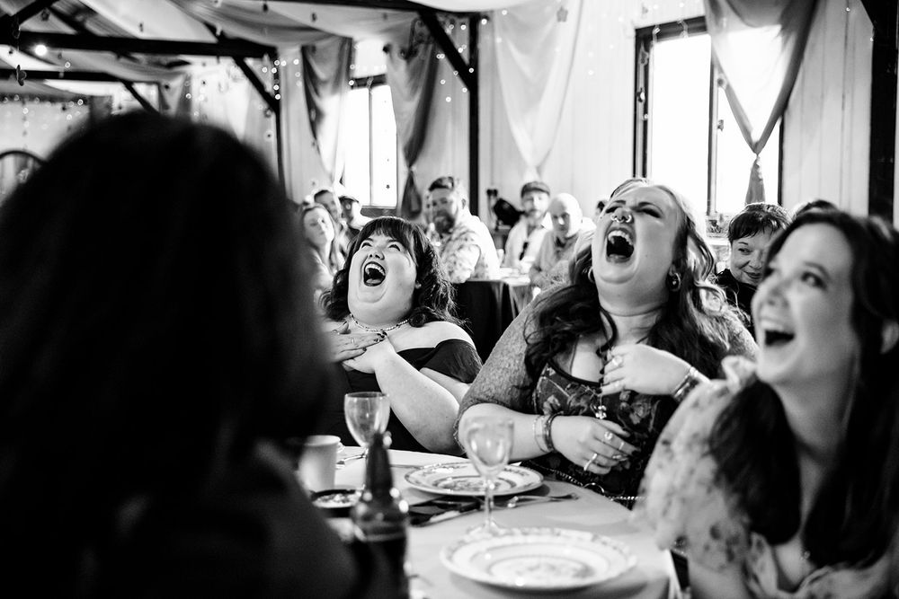 A black and white photo of guests laughing joyously at a social gathering around a table.