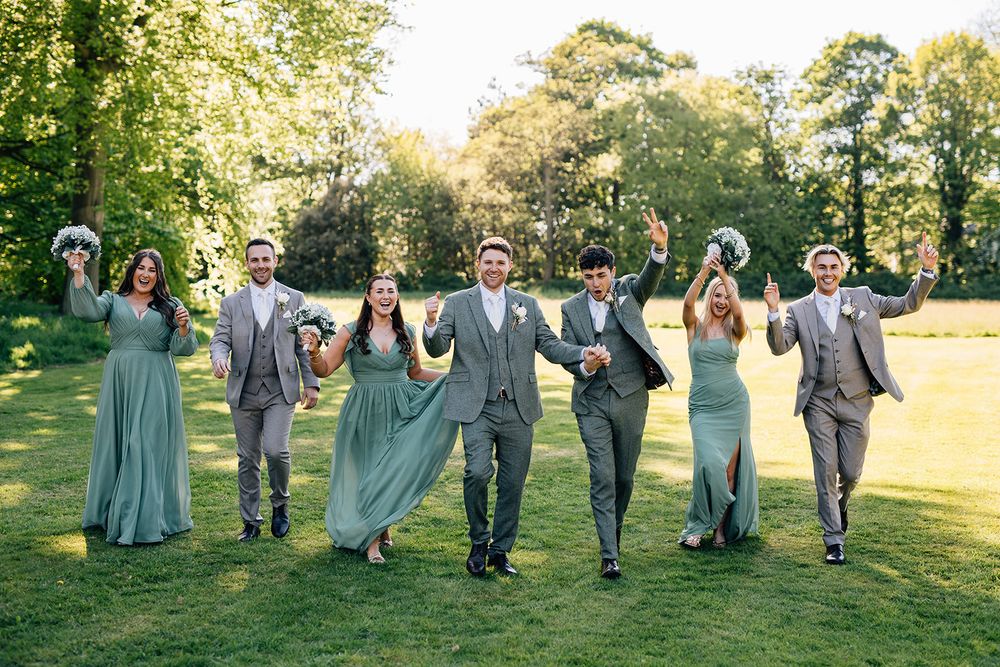 Wedding party members in gray and navy attire walk together across a sunny outdoor lawn during a summer celebration.