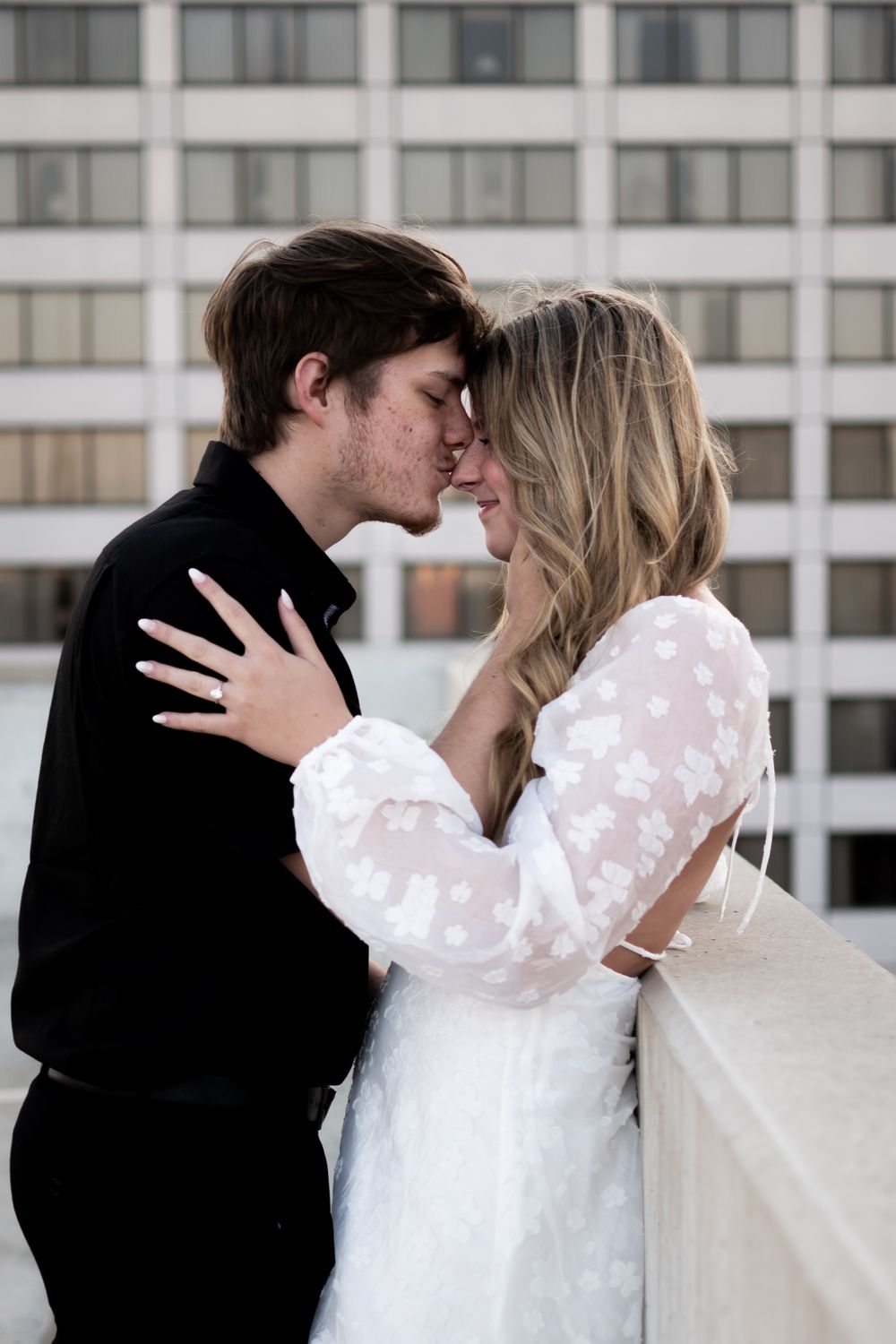 A romantic moment on a balcony as a couple in wedding attire share an intimate embrace against an urban backdrop. Ashley Enfield Photography
