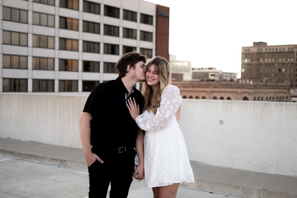 A couple shares an intimate moment together on a rooftop with urban buildings in the background.