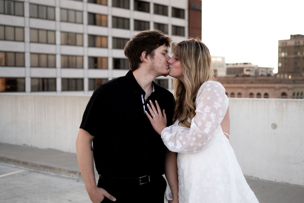 A romantic couple sharing a tender kiss on an urban rooftop with city buildings in the background.