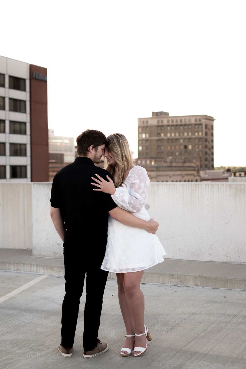 A couple shares a romantic moment on an urban rooftop with city buildings in the background. Ashley Enfield Photography