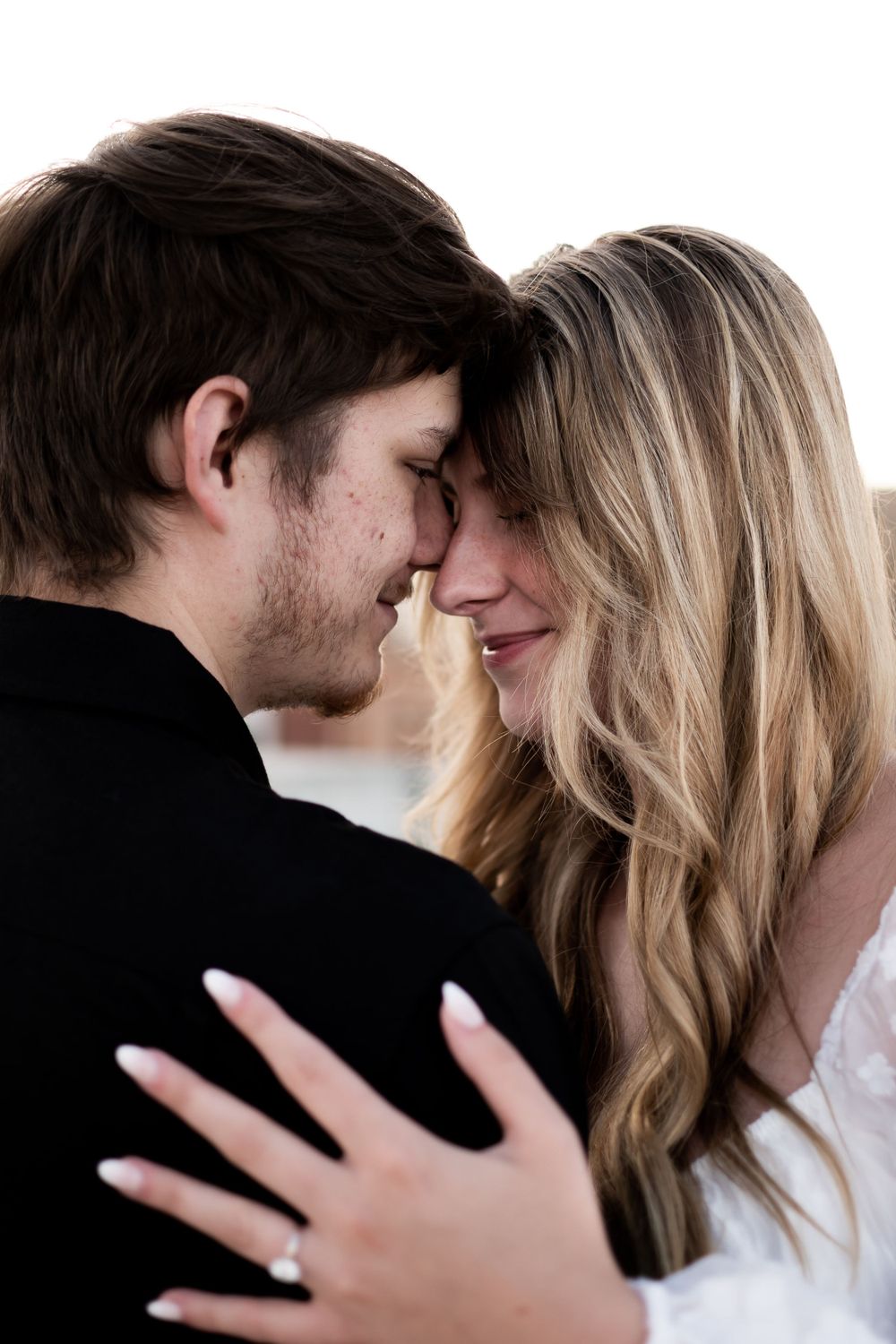 A tender romantic moment between a couple in black and white clothing as they embrace with their faces close together.