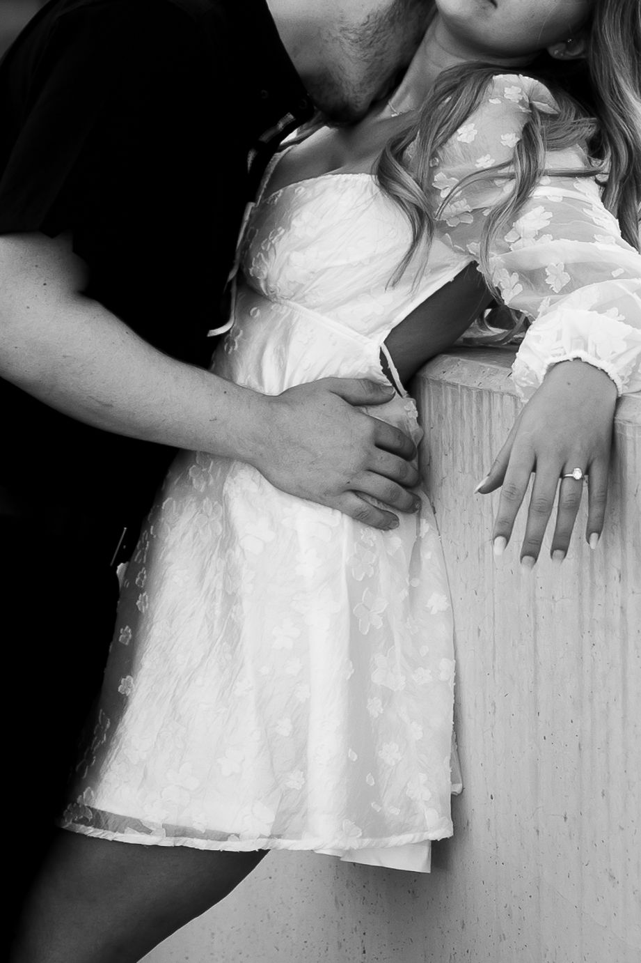 Black and white romantic photo showing someone in a white dress leaning against a light colored wall. Ashley Enfield Photography