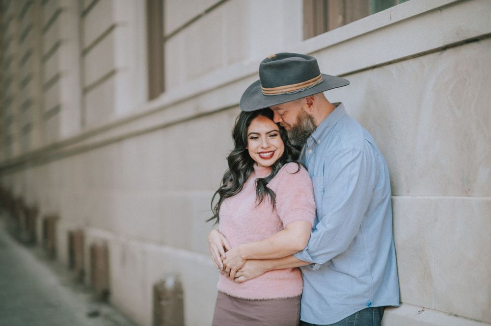 Couple sharing intimate moment against white building wall in urban setting.