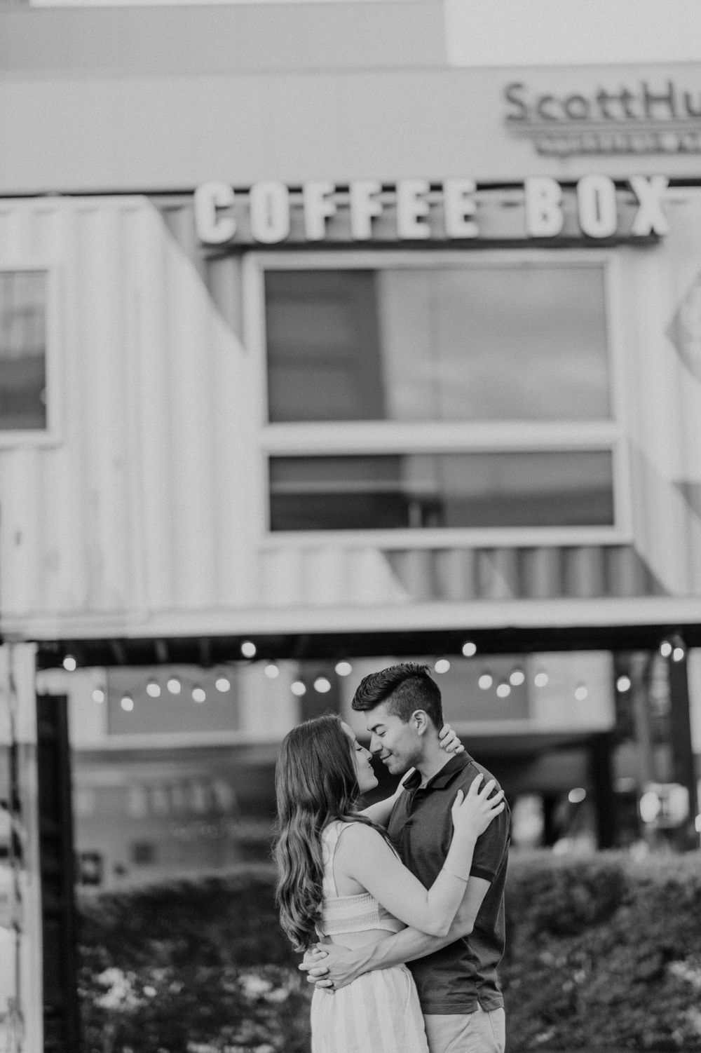 Couple embracing outside Coffee Box cafe with string lights in black and white photography.
