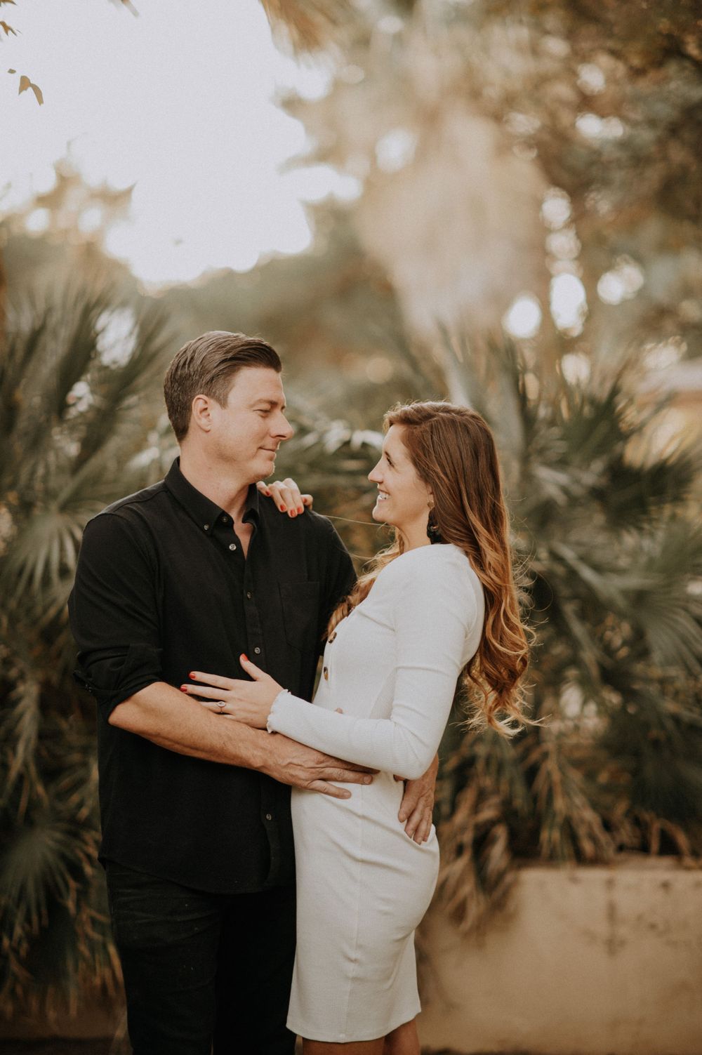 Couple sharing a romantic moment in front of tropical palm trees during sunset.