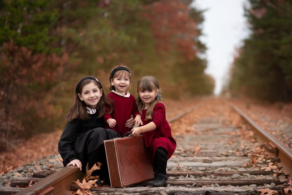 Small figures pose with a vintage suitcase on railroad tracks during fall season.