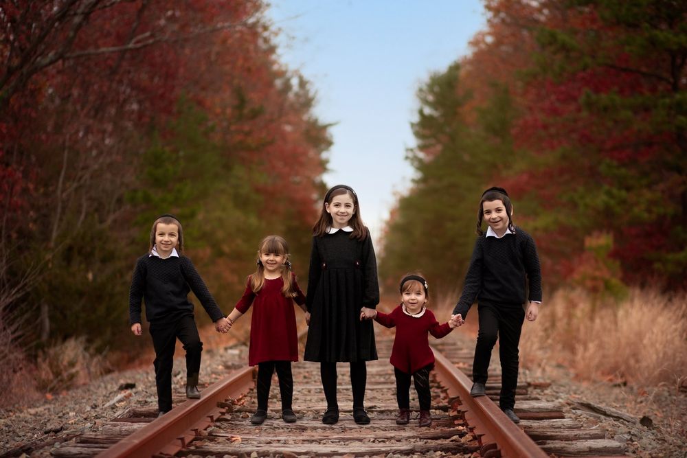 Silhouetted figures hold hands while standing on railway tracks between fall trees at dusk.