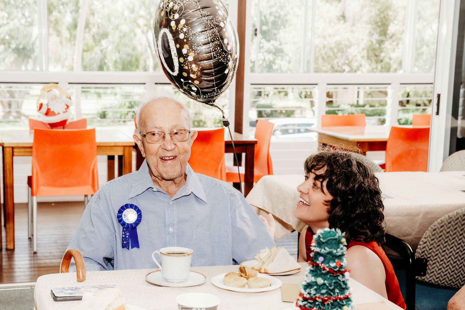 Senior residents gather around tables in a bright dining room for a social meal together.