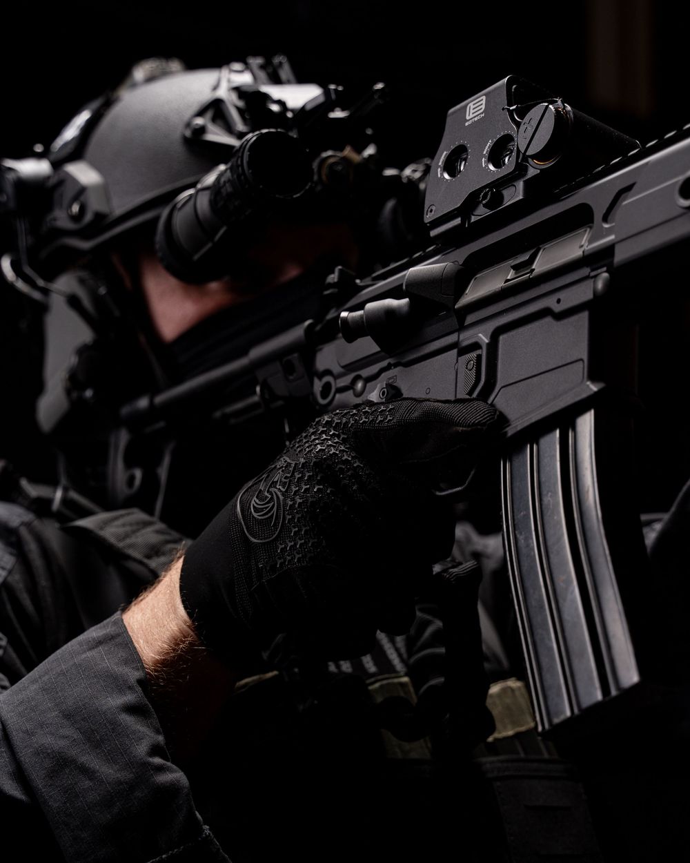 Close-up view of a black tactical rifle with scope in dark lighting conditions.