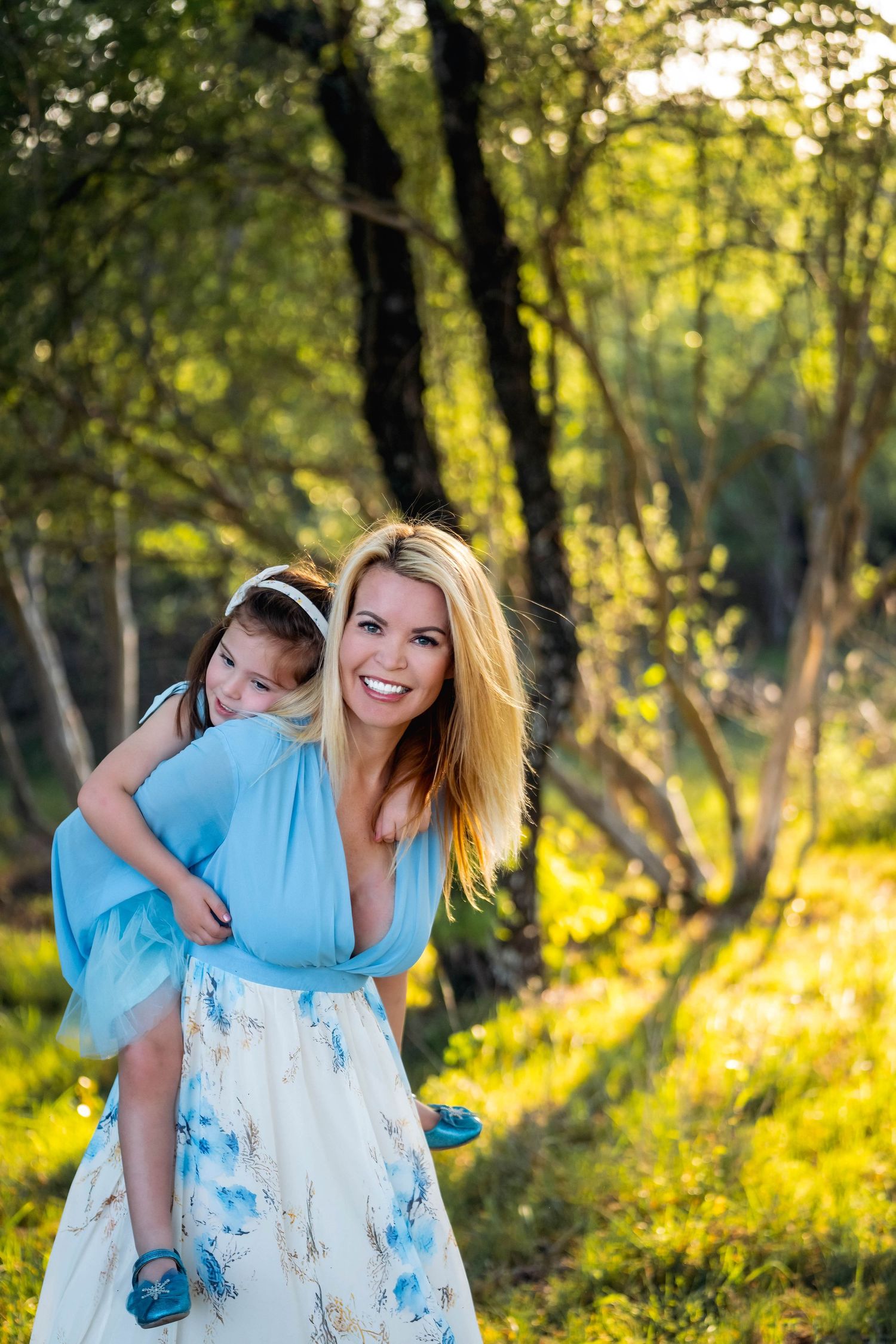 Expecting mother in flowing pink dress poses in sunlit garden setting.