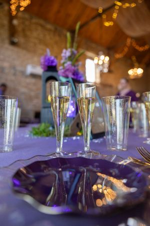 Elegant table setting with champagne flutes and purple decor featuring romantic bokeh lighting and floral centerpieces.