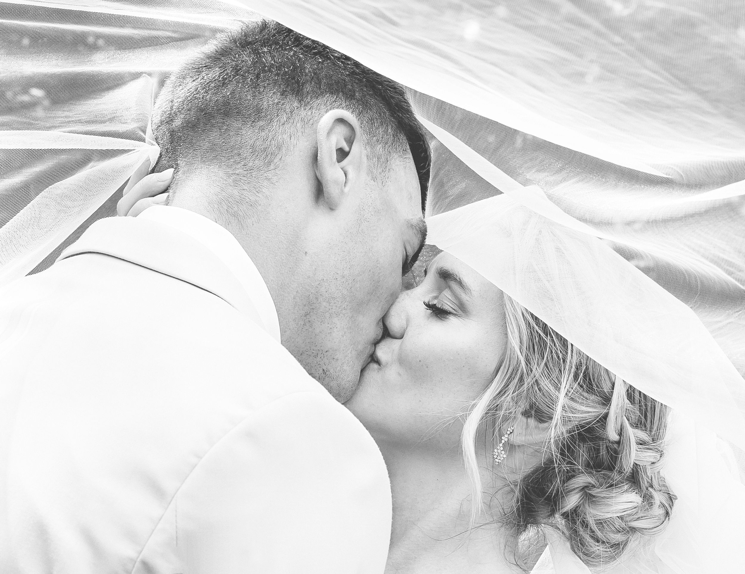 A romantic black and white photo series showing a couple embracing and kissing under a flowing veil.