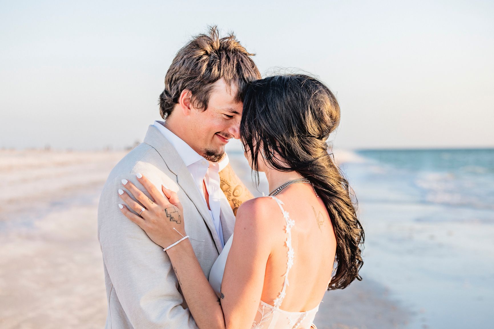 A couple shares a romantic moment in wedding attire, nearly kissing with ocean waves in the background. Florida beach destination wedding