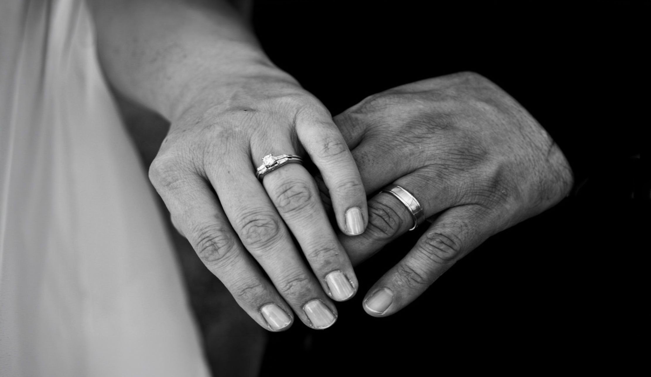 Black and white close-up of hands with wedding rings in a romantic and artistic composition.