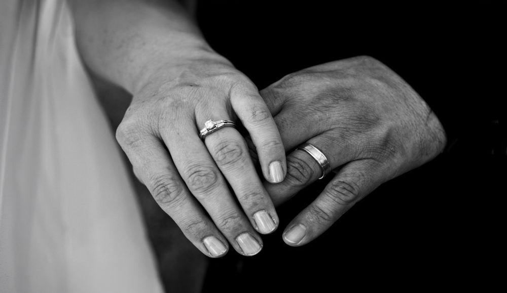 Black and white close-up of hands with wedding rings in a romantic and artistic composition.