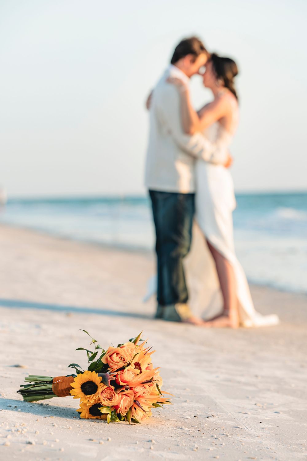 A wedding bouquet of sunflowers and roses on a beach with a couple kissing in the background.
Florida beach destination wedding