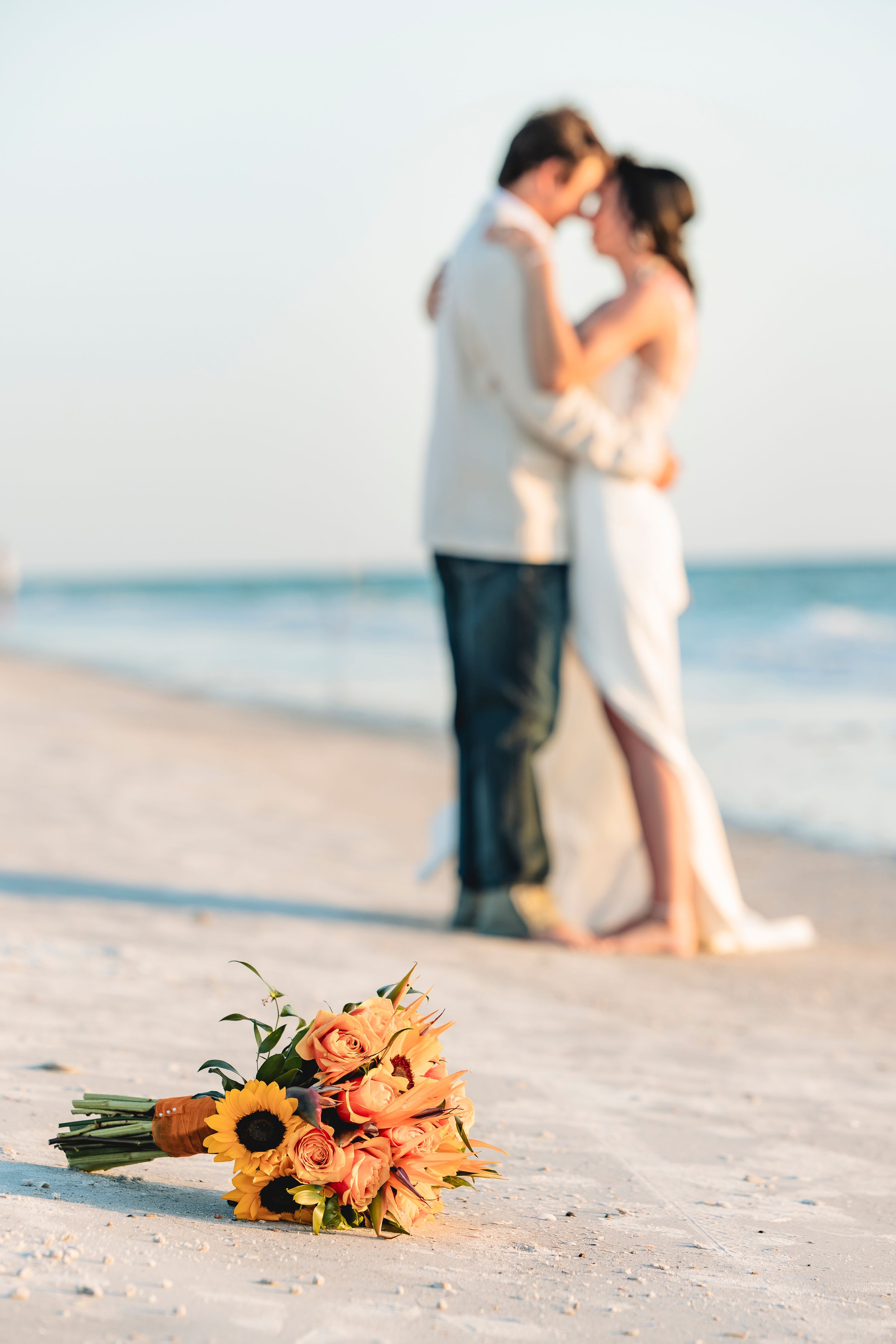 A wedding bouquet of sunflowers and roses on a beach with a couple kissing in the background.
Florida beach destination wedding