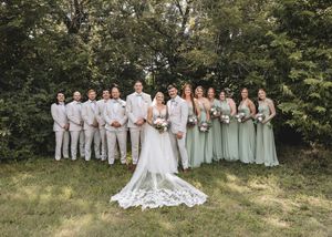 Wedding party in white and sage green dresses poses together on grassy hillside for outdoor group photos.