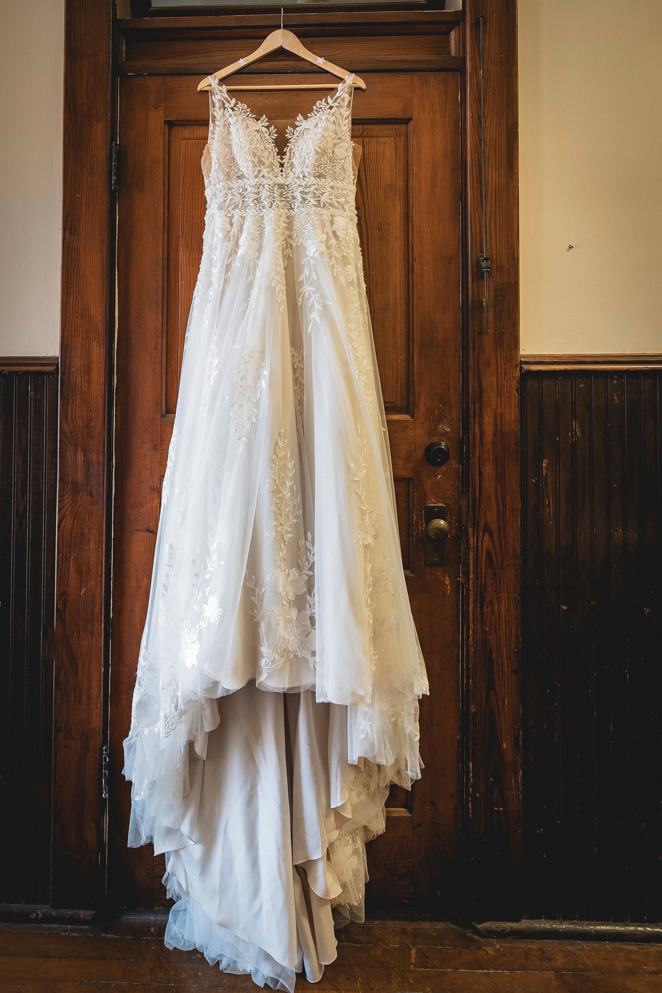 A white lace wedding dress hangs elegantly on display against dark wooden doors creating a striking contrast.