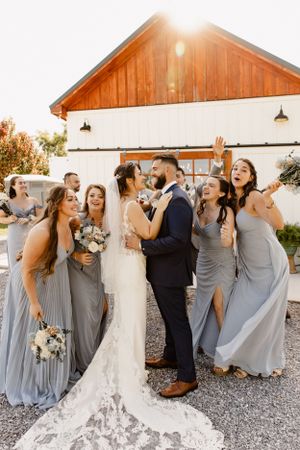 Bridal party in grey dresses laughing together outside rustic barn venue.
